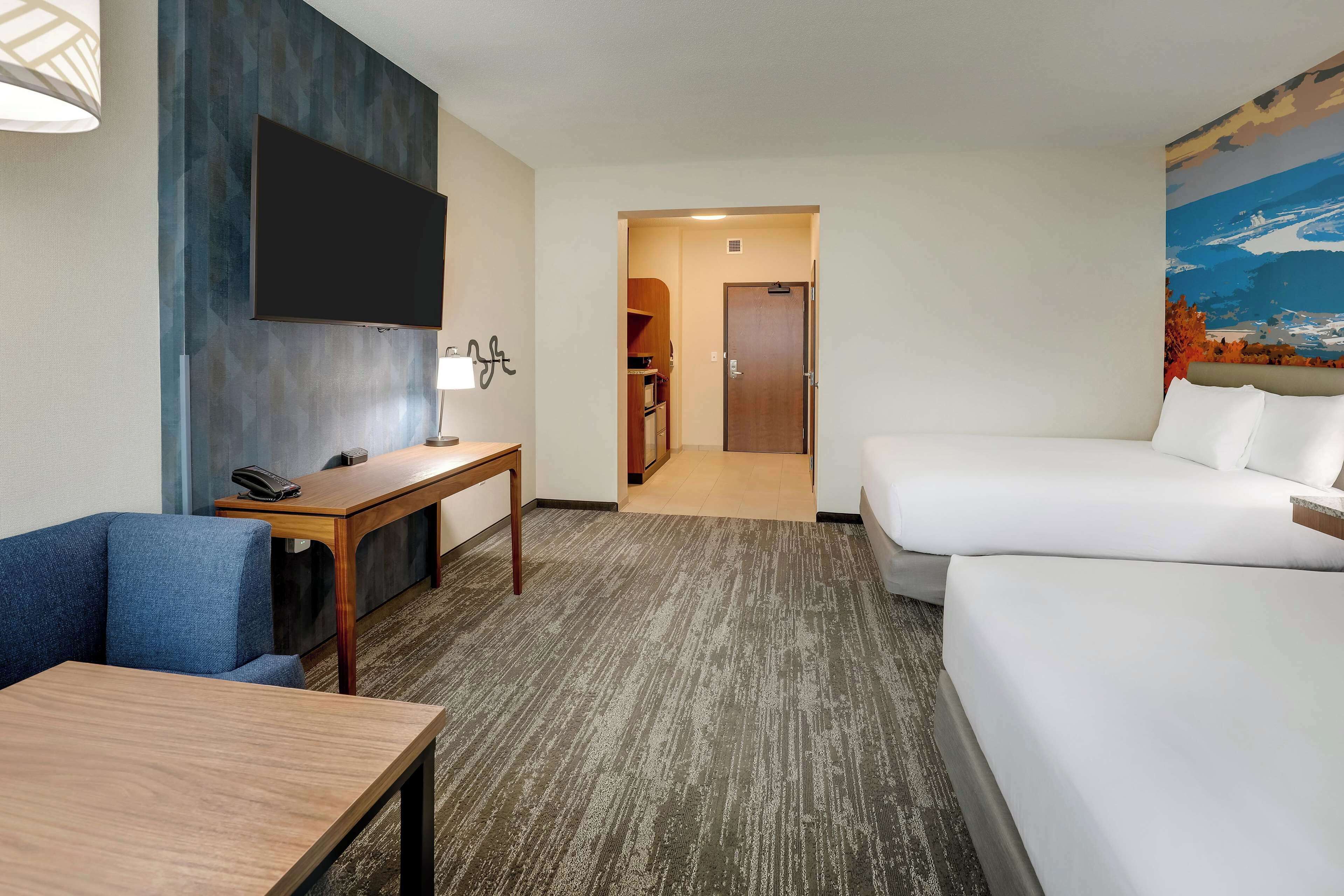 Habitación de hotel con una cama grande, un escritorio con teléfono, un televisor de pantalla plana en la pared y piso alfombrado.