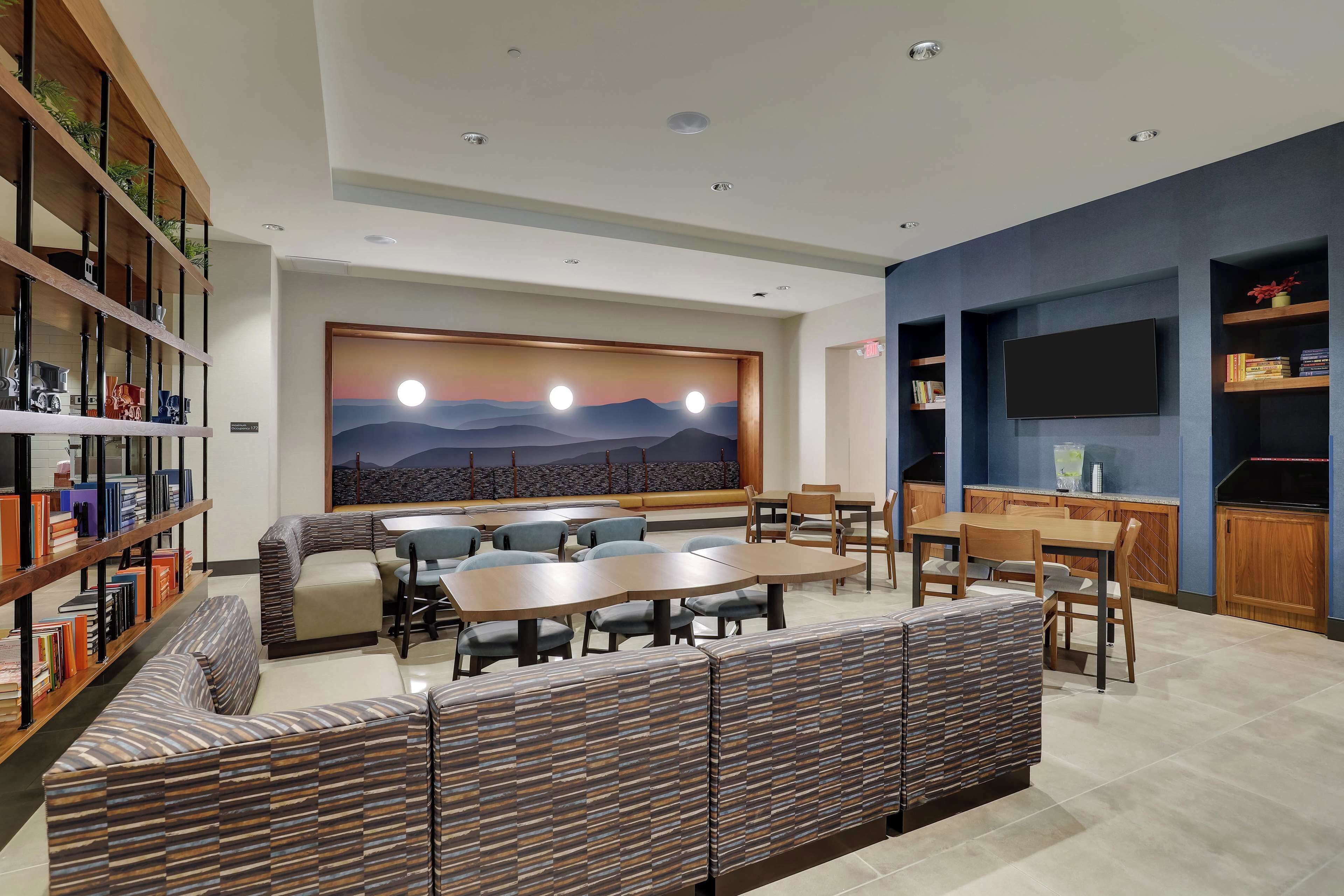 A modern lounge area with a large wall mural, seating arrangements, and a flat-screen TV.