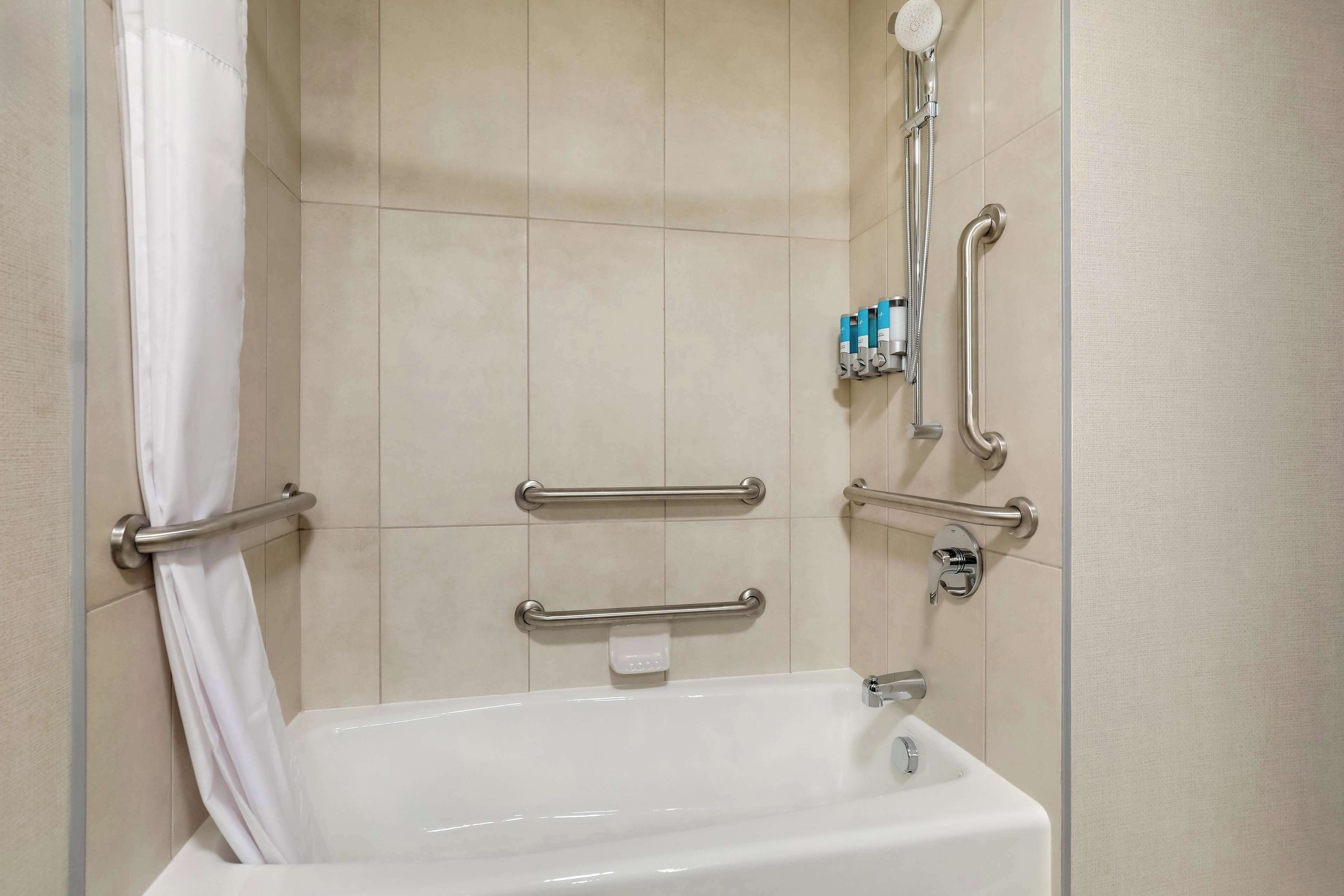 A bathroom with a bathtub, grab bars, and a showerhead.