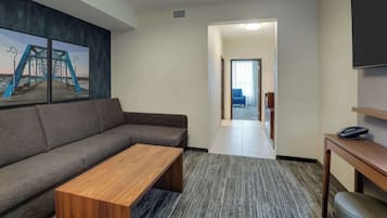 A modern hotel room with a gray sofa, a wooden coffee table, and a large painting of a bridge.