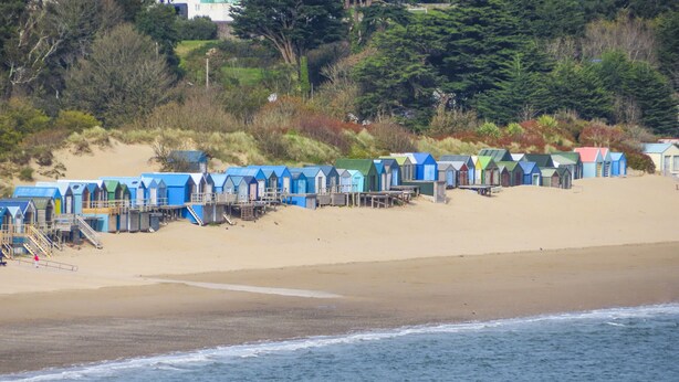 A row of beach huts with wooden stairs leading up to them, situated on a sandy beach with a view of the ocean. - 15 Maes Awel (Pwllheli)