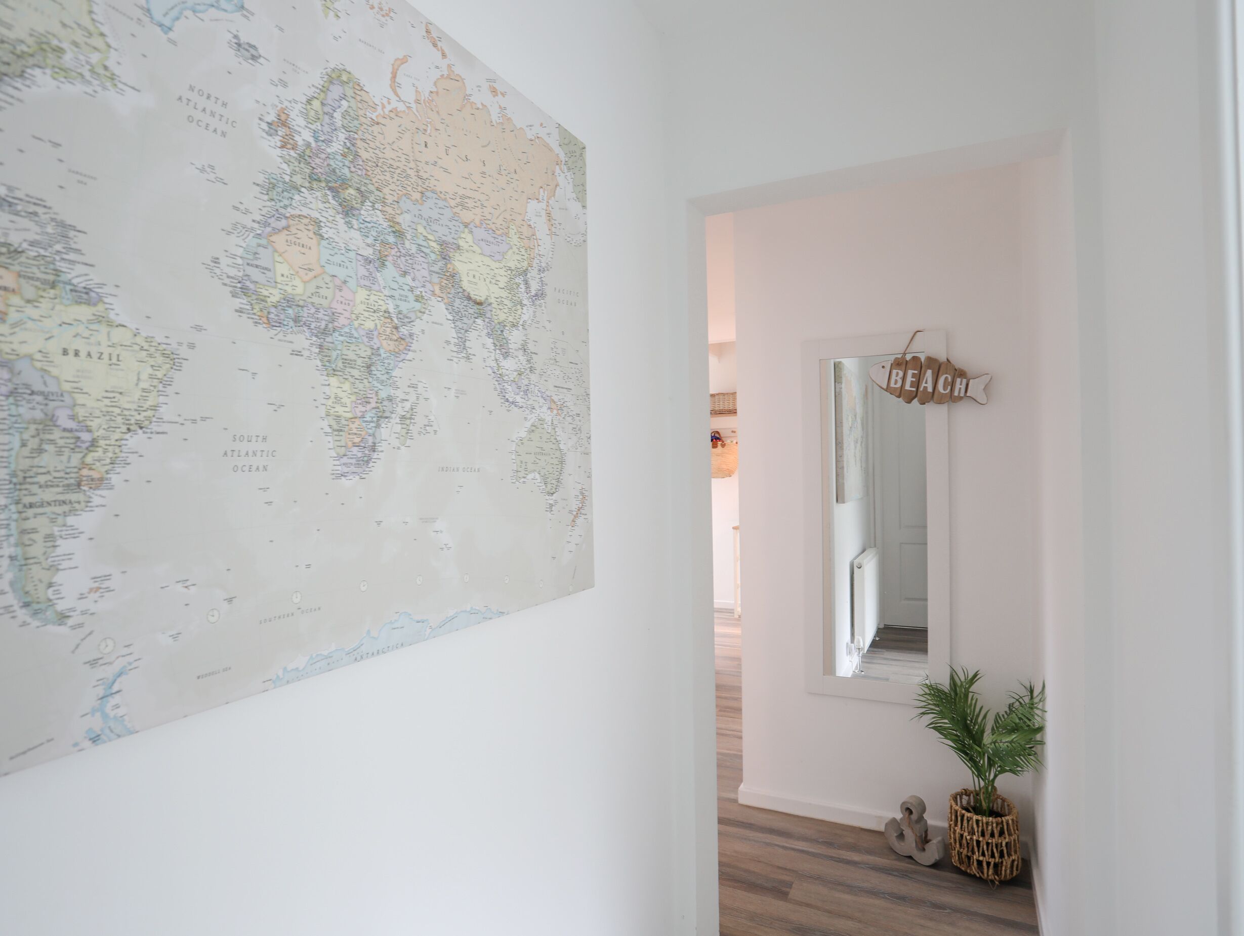 A hallway with a large world map on the left wall, a mirror on the right, and a small plant in a woven basket.