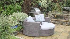 A patio with a round wicker sofa, a grill, and a bird feeder. - 15 Maes Awel (Pwllheli)