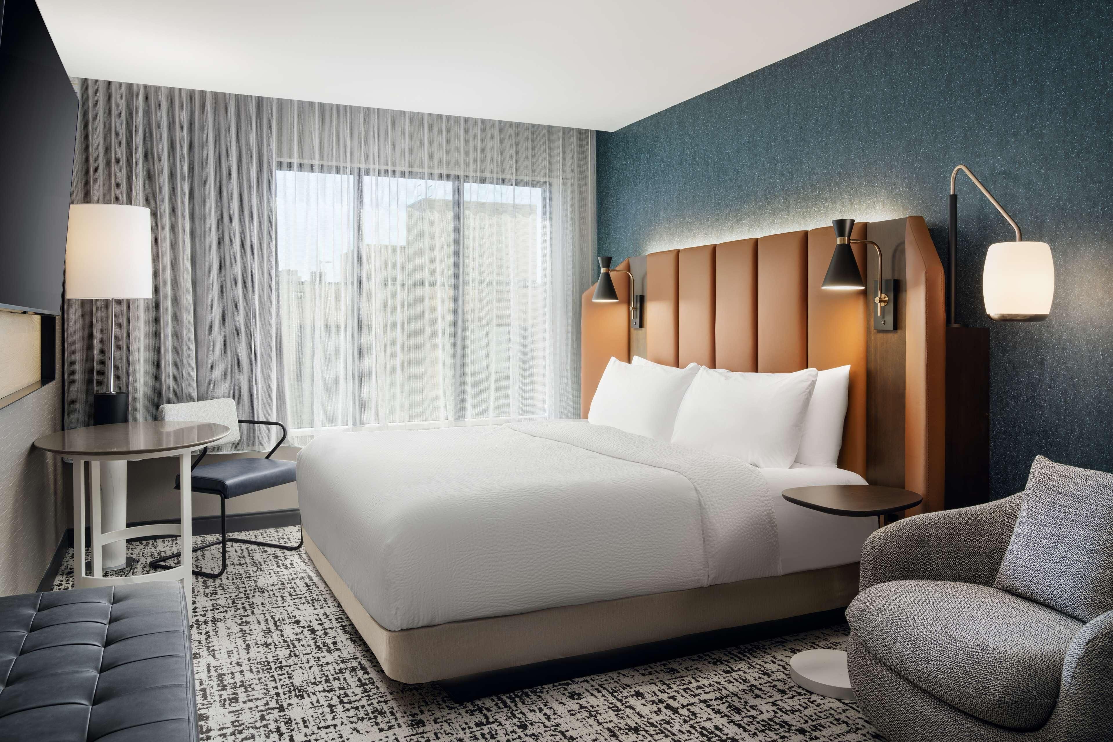 A modern hotel room with a large bed, a desk, a chair, and a sofa.