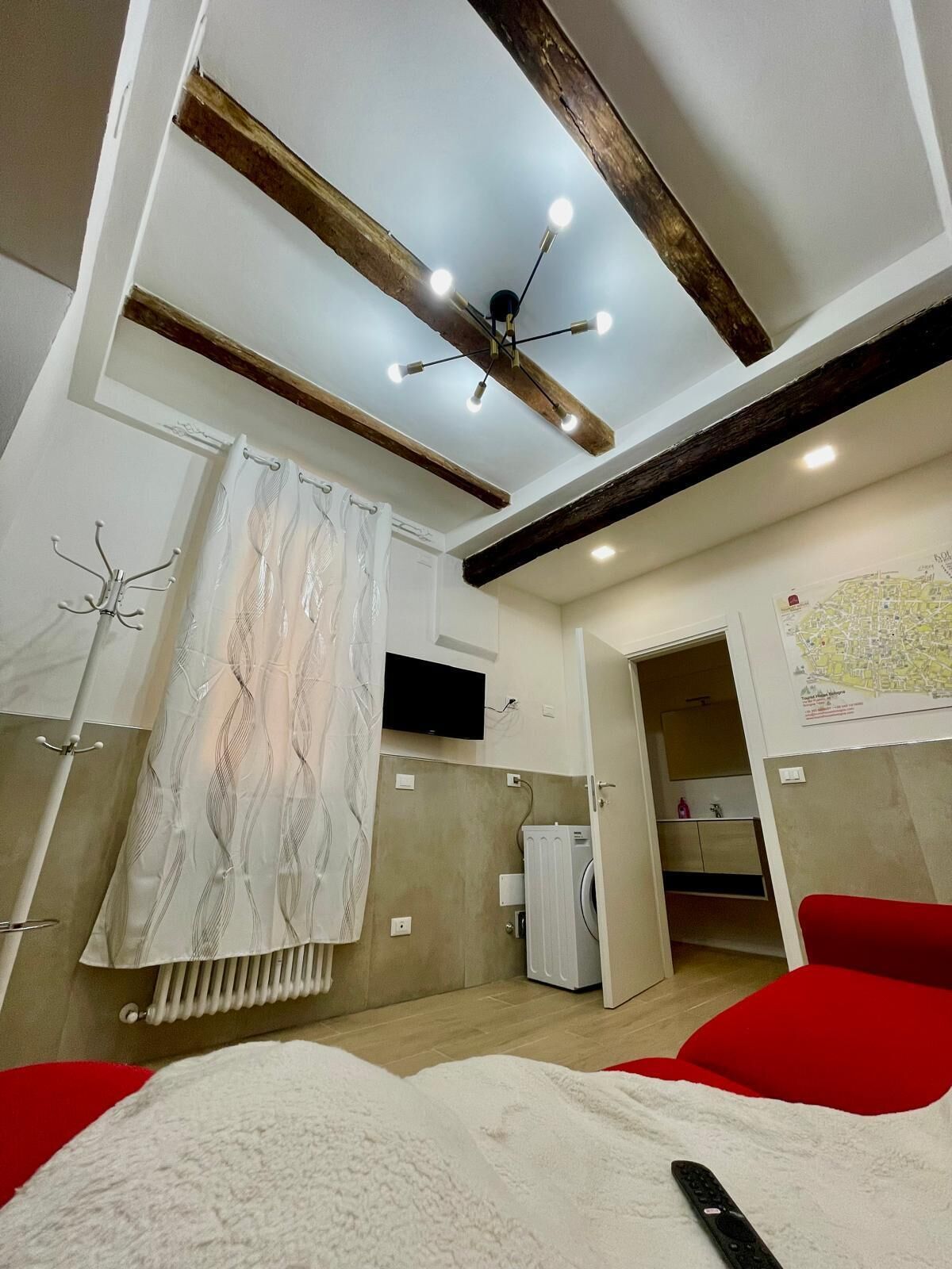 A modern hotel room with a bed, a red chair, a ceiling fan, a TV, and a map on the wall.