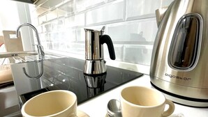 A modern kitchen with a black induction cooktop, a stainless steel coffee maker, and two white cups with saucers. - 50 Tourist House Bologna Pratello Garden (Bologna)