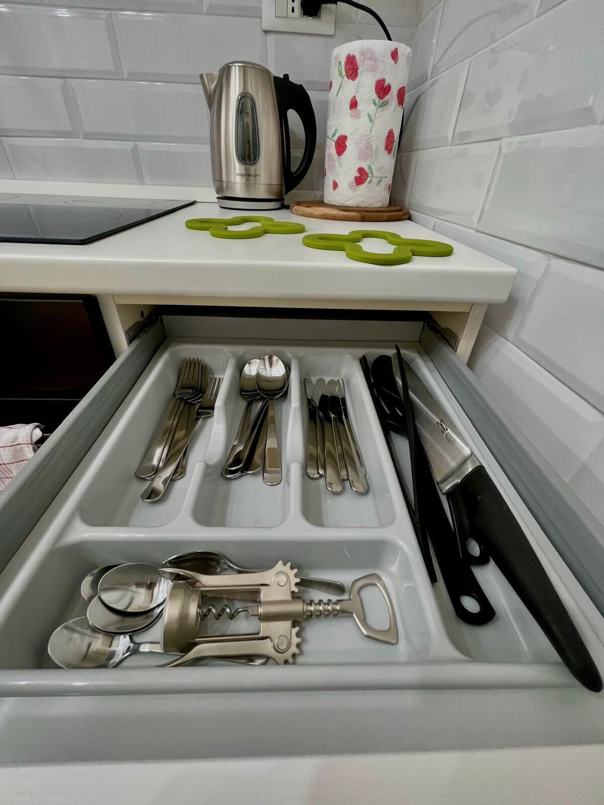 A kitchen drawer with utensils neatly organized, a kettle, and a floral towel on the countertop.