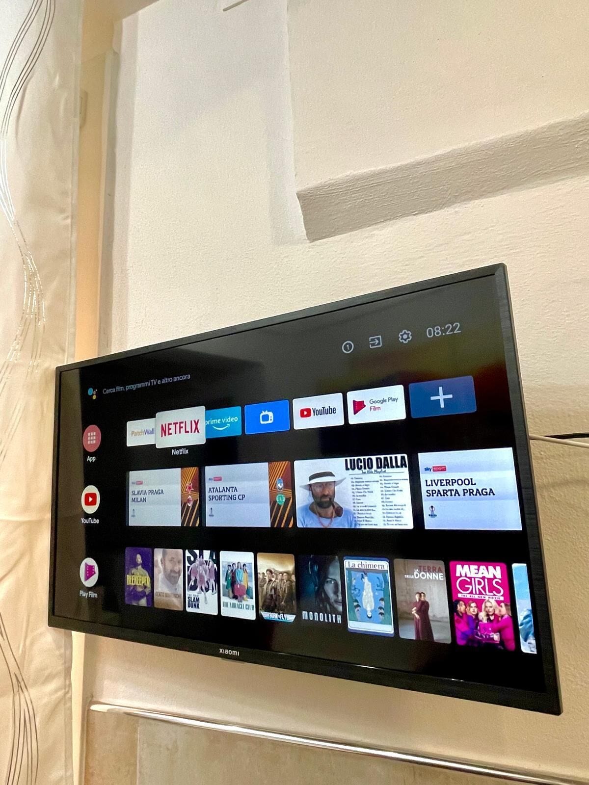 Televisor de pantalla plana montado en la pared mostrando una interfaz de servicio de streaming con diversas opciones de contenido.