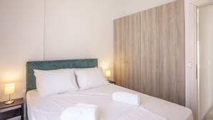 Un letto rifatto con lenzuola bianche e due cuscini, una lampada da comodino e un armadio in legno.