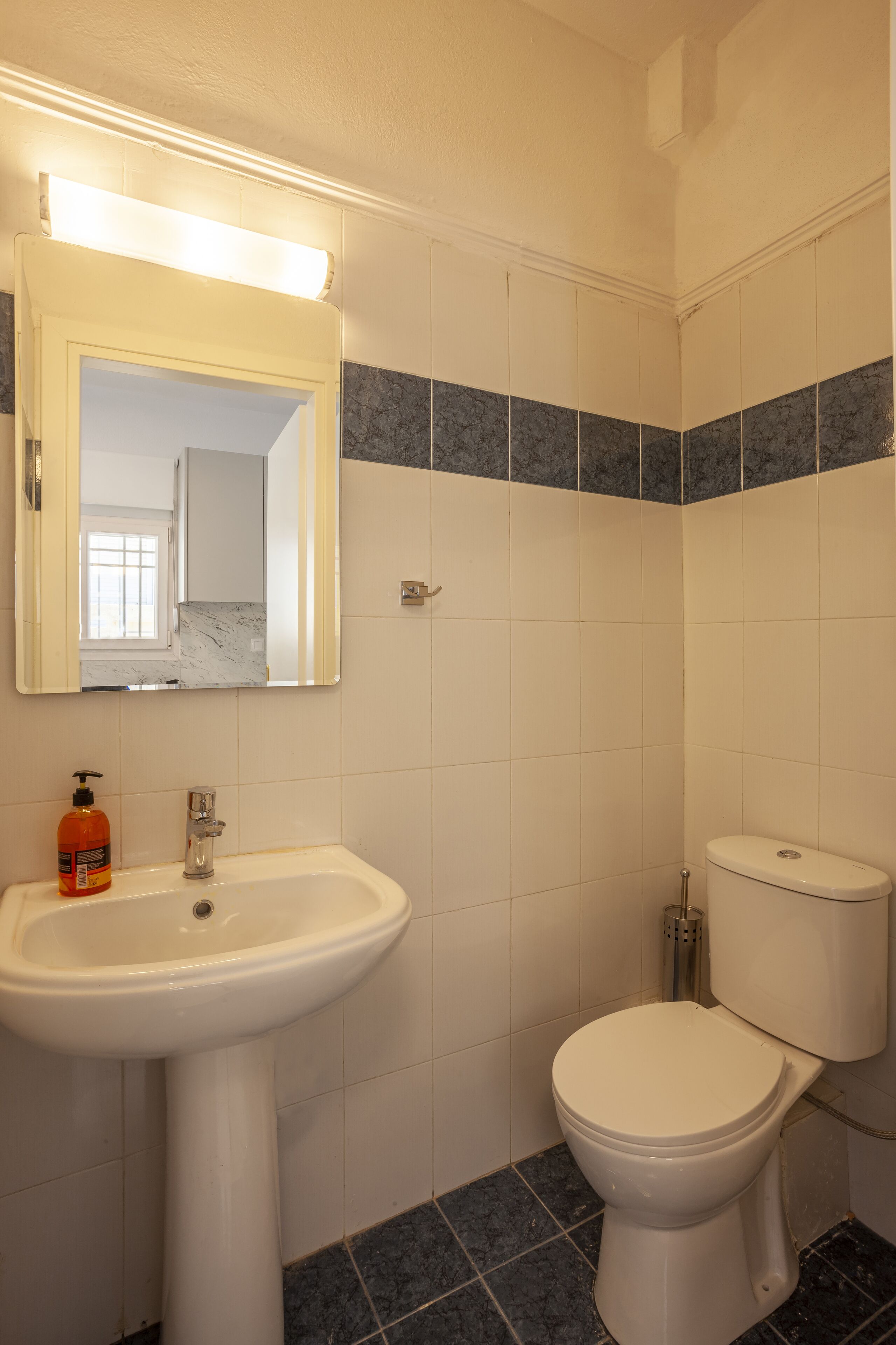 Un baño con un lavamanos blanco, un espejo, un inodoro y azulejos azul oscuro.