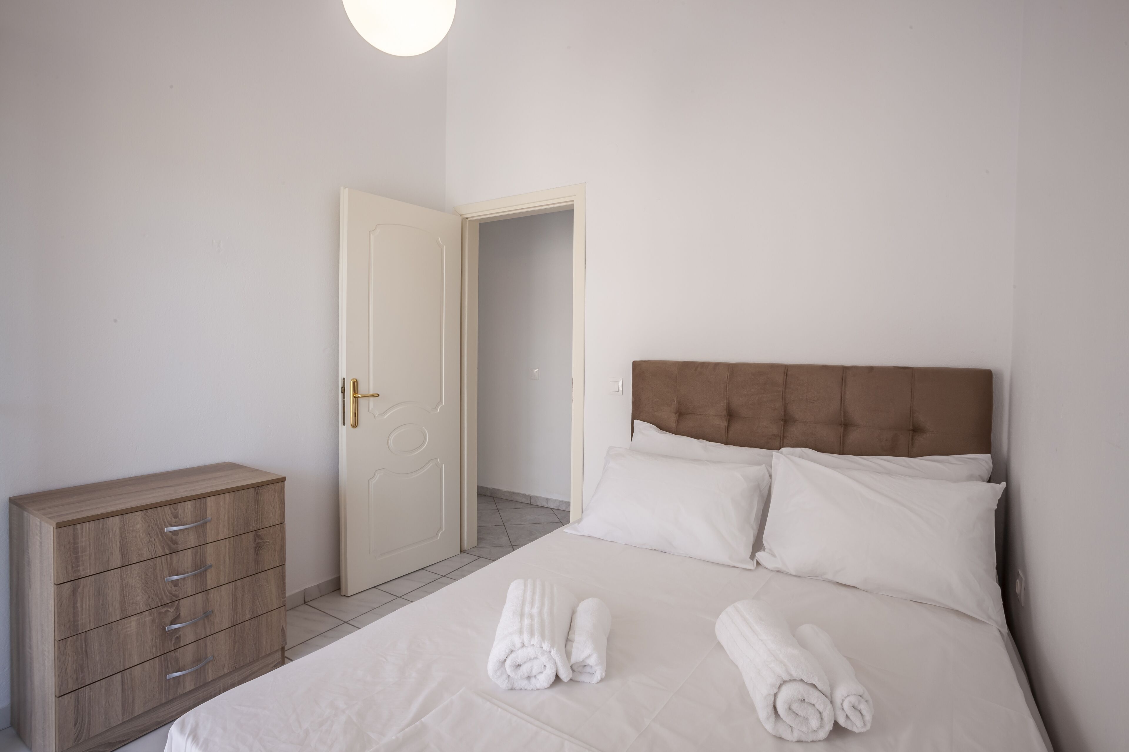 Une chambre d’hôtel avec un lit, deux oreillers, une commode en bois et une porte.