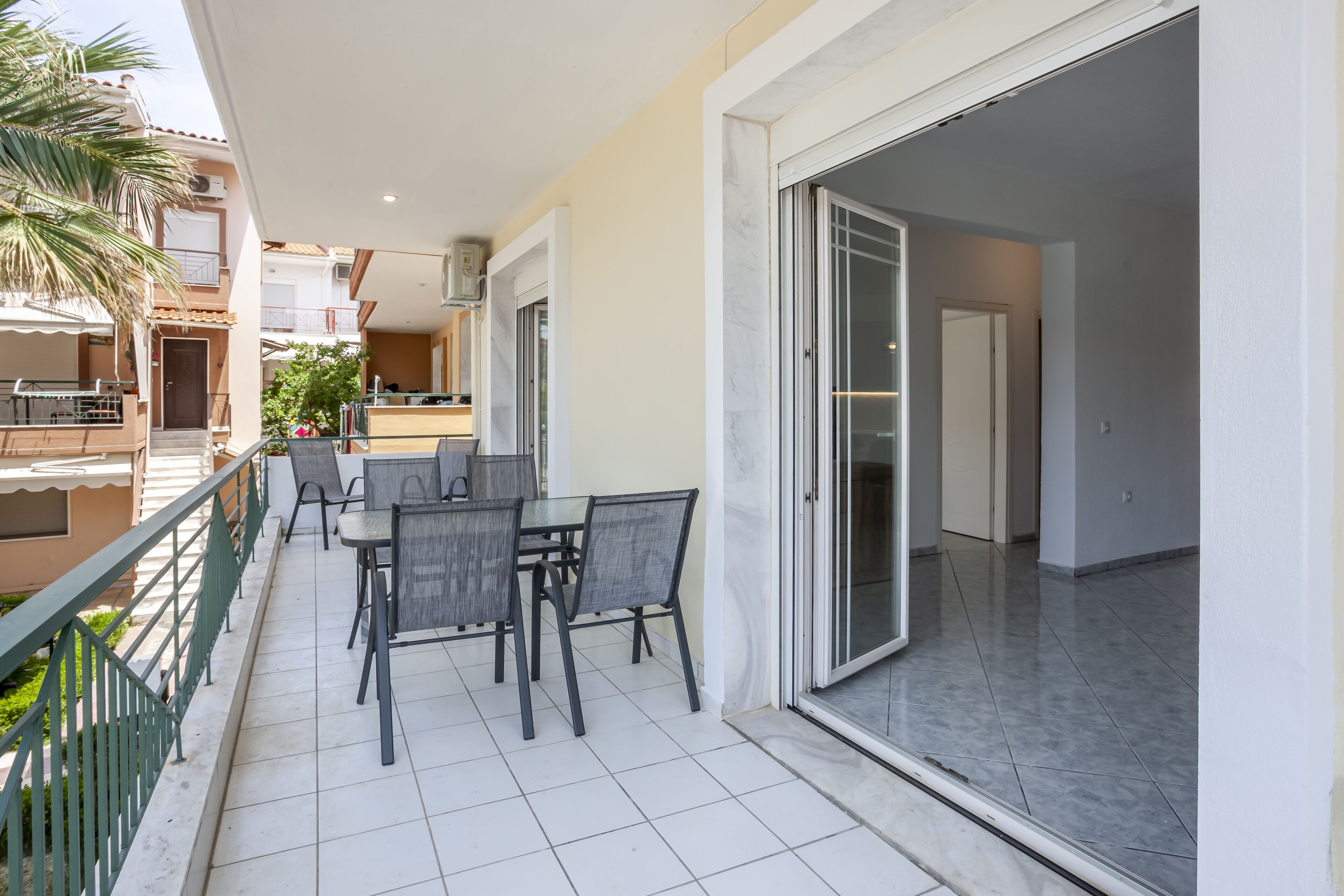 A balcony with a dining table and chairs, a sliding glass door, and a view of a building with balconies.