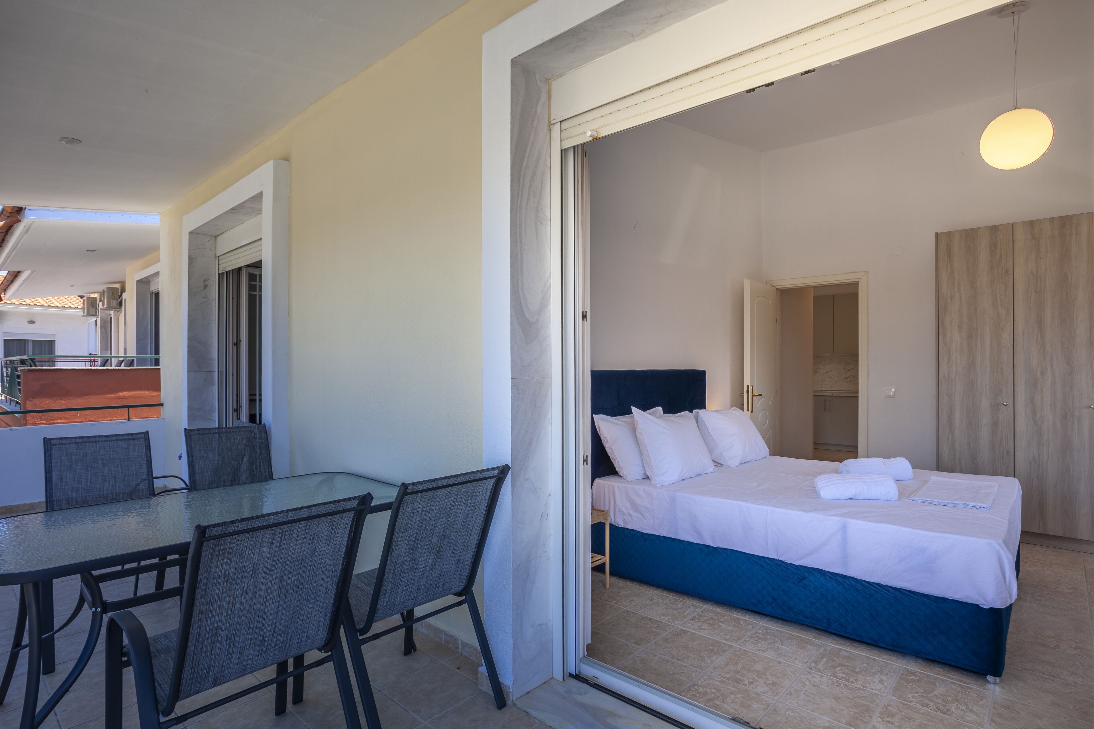 A hotel room with a bed, a glass table with chairs, and a view of the balcony.