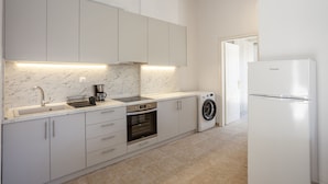 A modern kitchen with white cabinets, a built-in oven, a washing machine, and a refrigerator. - Aris Luxury Apartments (Kassandra)