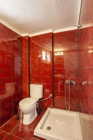 A bathroom with a toilet, shower, and red tiled walls. - Aris Luxury Apartments (Kassandra)