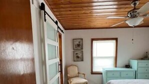 A bedroom with a wooden ceiling, a bed, a chair, a dresser, and a window. - Beachside Retreat (North Myrtle Beach)