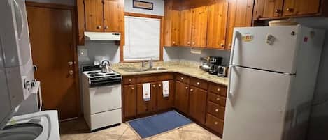 A compact kitchen with wooden cabinets, a white stove, a sink, and a refrigerator.