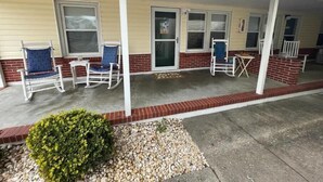 A covered porch with white rocking chairs and a small bush. - Beachside Retreat (North Myrtle Beach)
