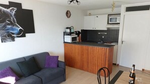Un appartamento moderno con un divano grigio, un tavolo da pranzo in legno e un angolo cottura con mobili bianchi e un forno a microonde.