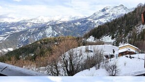 Paesaggio montano innevato con una baita di legno e una seggiovia in primo piano.
