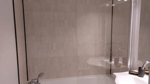 Un bagno moderno con doccia vetrata, lavandino bianco e pareti inferiori rivestite di piastrelle verdi.