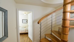 Una escalera de madera con barandillas de metal que lleva a un dormitorio con una cama y un cuadro en la pared.