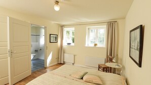 Un dormitorio con cama, una silla, una mesa, una ventana y una puerta que da a un baño.