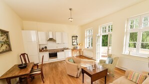 A spacious living area with a kitchen, wooden flooring, and large windows. - Apartment 'Gut Grubnow Rügen - Ferienwohnung 7' with Lake View, Shared Garden and Wi-Fi (Neuenkirchen)