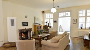 A living room with a fireplace, a sofa, a dining table, and a chandelier. - Apartment 'Gut Grubnow Rügen - Ferienwohnung 7' with Lake View, Shared Garden and Wi-Fi (Neuenkirchen)