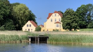 A lakeside property with a dock, two houses, and surrounding greenery. - Apartment 'Gut Grubnow Rügen - Ferienwohnung 7' with Lake View, Shared Garden and Wi-Fi (Neuenkirchen)