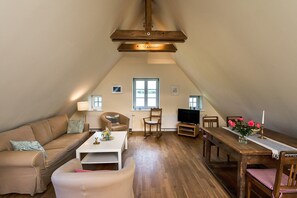 A cozy loft-style living room with a high ceiling, a wooden dining table, a sofa, a coffee table, and a television.