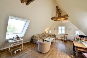 A loft-style room with a sloped ceiling, a sofa, a coffee table, a wooden bench, and a dining table.
