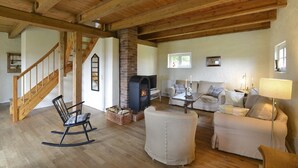 Un salón espacioso con escalera de madera, chimenea, un conjunto de sofás y una mecedora.