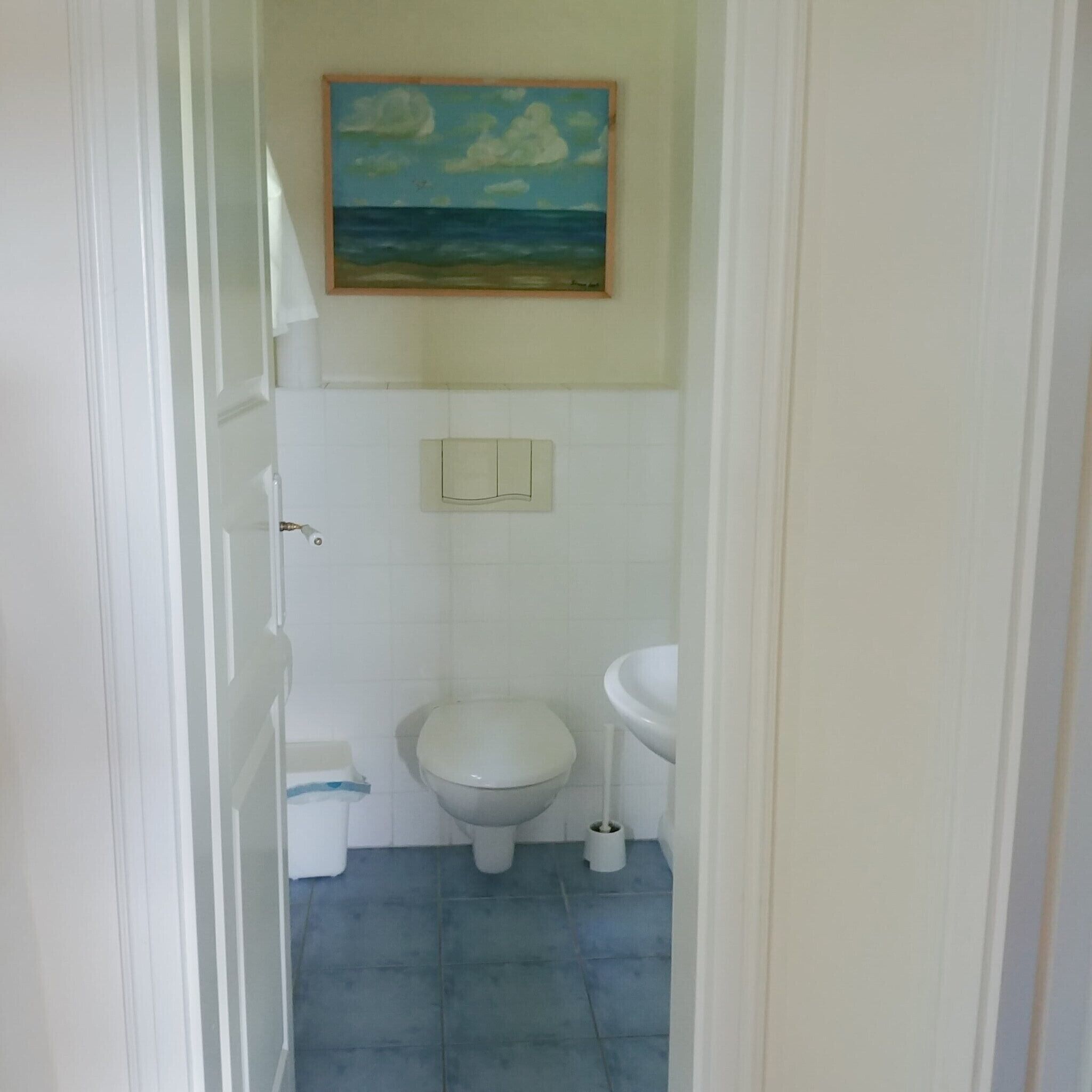 Un baño pequeño con inodoro, lavamanos y un cuadro de una playa en la pared.