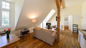 Une pièce de style « loft », avec un plafond en pente, un canapé, une table avec une lampe et une vue sur l’extérieur.