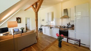 Une cuisine moderne avec des meubles blancs, une cuisinière et un évier. On y trouve un coin repas avec un canapé et une table, ainsi qu'une poutre en bois au plafond.
