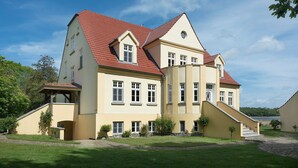 A large, two-story building with a red-tiled roof, multiple windows, and a central staircase. - Holiday Apartment "Gut Grubnow Rügen - 1" with Lake View, Shared Garden & Wi-Fi (Neuenkirchen)
