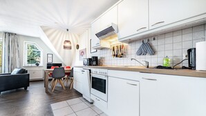 Et moderne køkken med hvide skabe, indbygget ovn samt spiseområde med bord og stole.