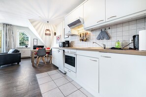Moderni keittiö, jossa on valkoiset kaapit, sisäänrakennettu uuni sekä ruokailutila, jossa on pöytä ja tuolit.