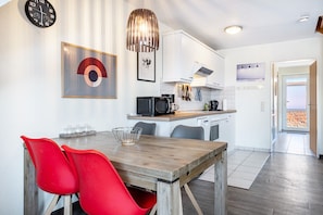 Une cuisine moderne avec des meubles blancs, un four à micro-ondes et un coin repas comprenant une table en bois et des chaises rouges.