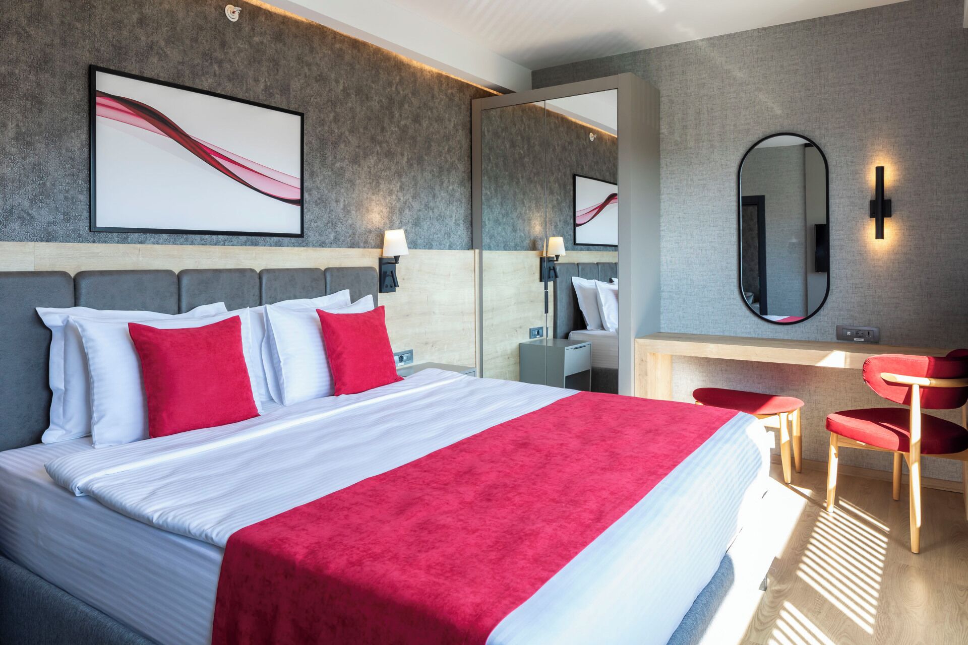 Habitació d'hotel moderna amb un llit gran, una tocador amb mirall i una paret vermella d'accentuació.