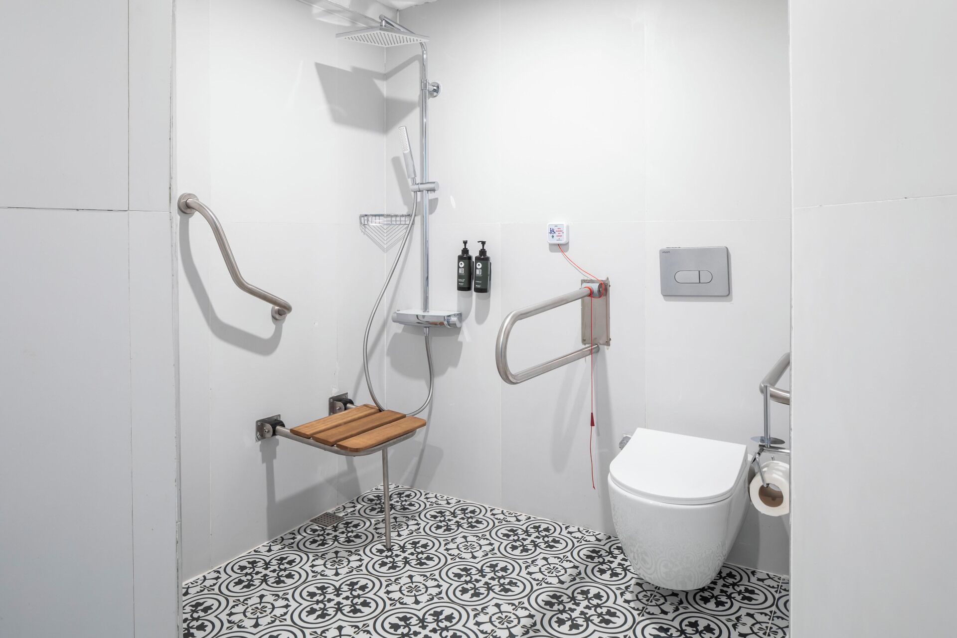 A small, white bathroom with a shower, toilet, and a wooden bench.