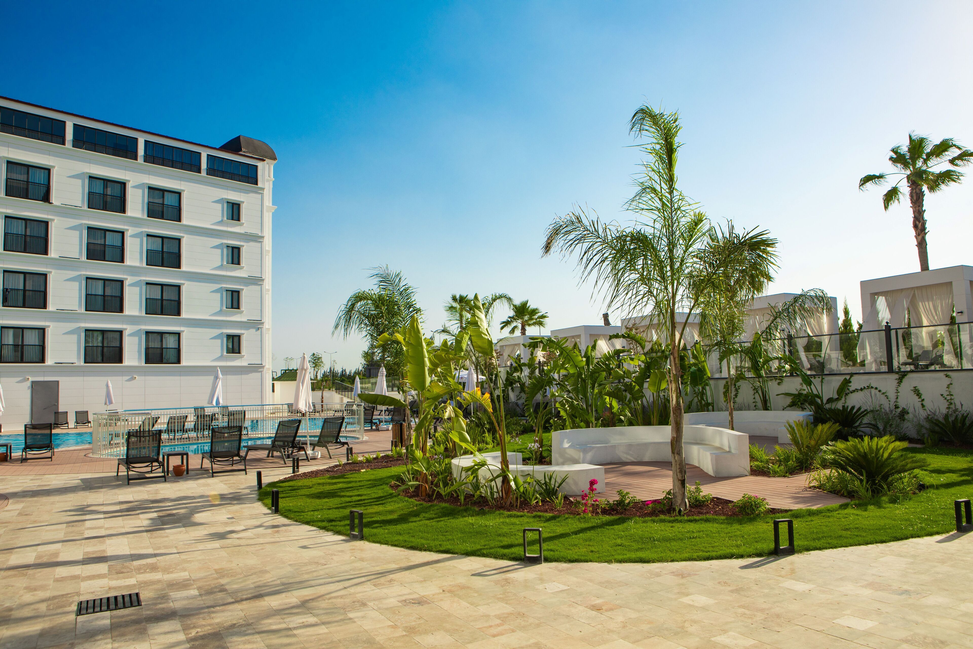 Ein Hotelinnenhof mit Swimmingpool, Sitzgelegenheiten im Freien und Palmen.