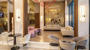 Een moderne hotellobby met een centrale zithoek, een televisiescherm en een decoratief plafond.