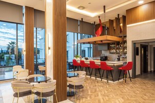 A modern bar area with a bar counter, red bar stools, and a view of the cityscape through large windows.