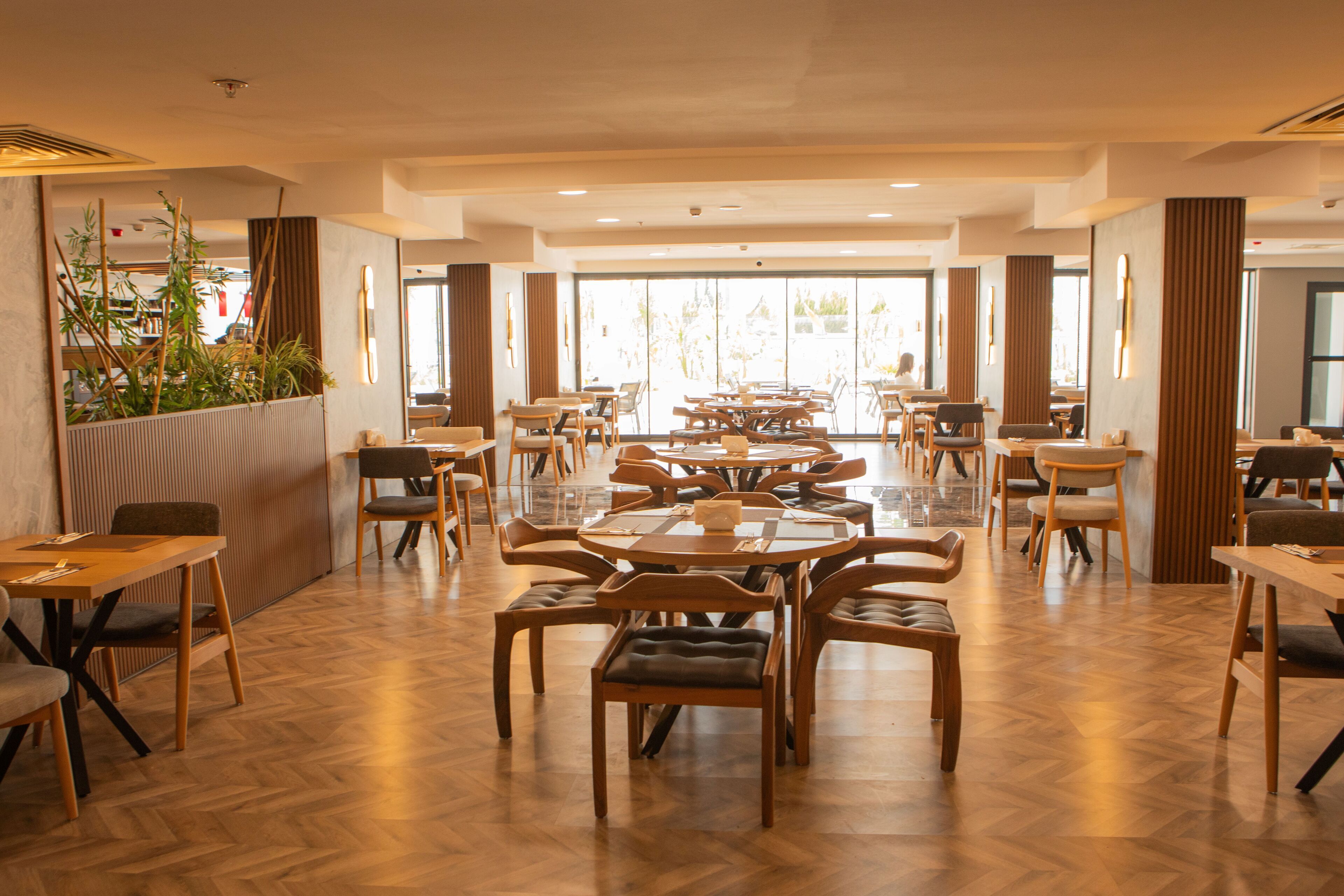 Un comedor amplio con varias mesas y sillas, ventanas grandes y piso de madera.
