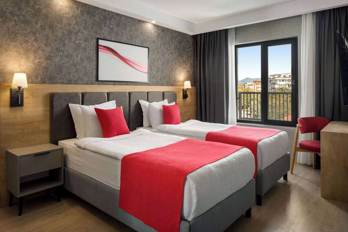 Hotelkamer met twee bedden, een bureau, een stoel, een televisie en een balkon met uitzicht.