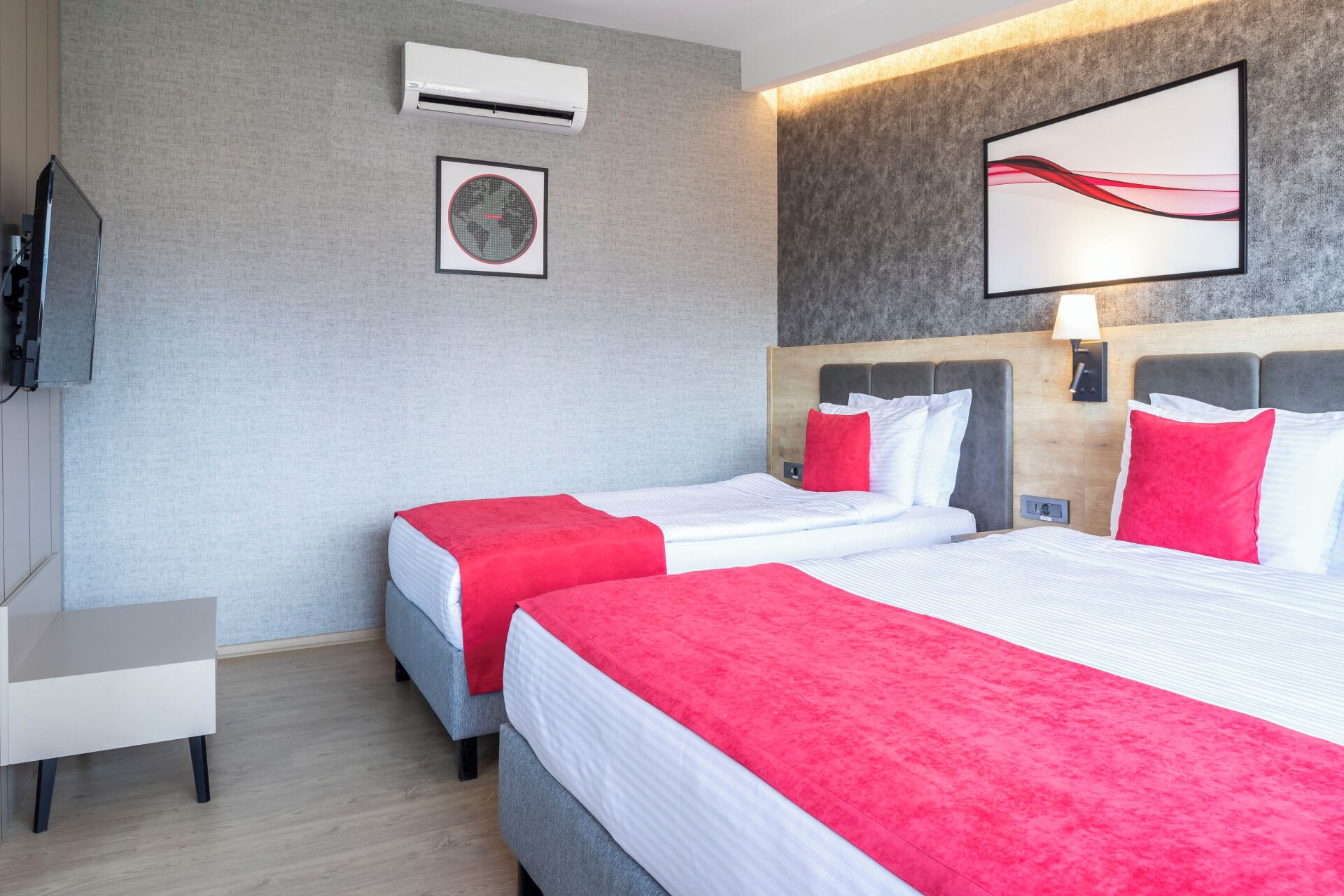 Ein Hotelzimmer mit zwei Betten, einem Fernseher, einer Klimaanlage, einem gerahmten Bild und einer Wandleuchte.