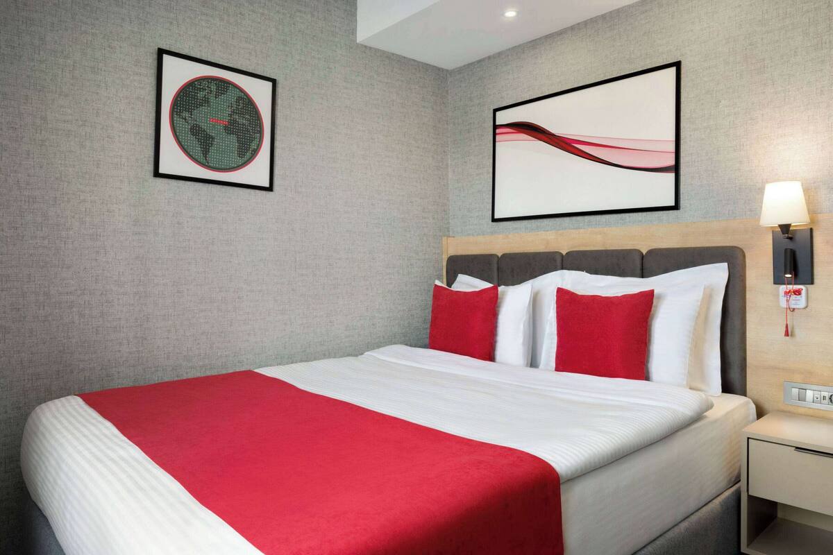 Hotelkamer met een groot bed, een hoofdbord, een nachtkastje, een wandlamp en twee ingelijste kunstwerken.