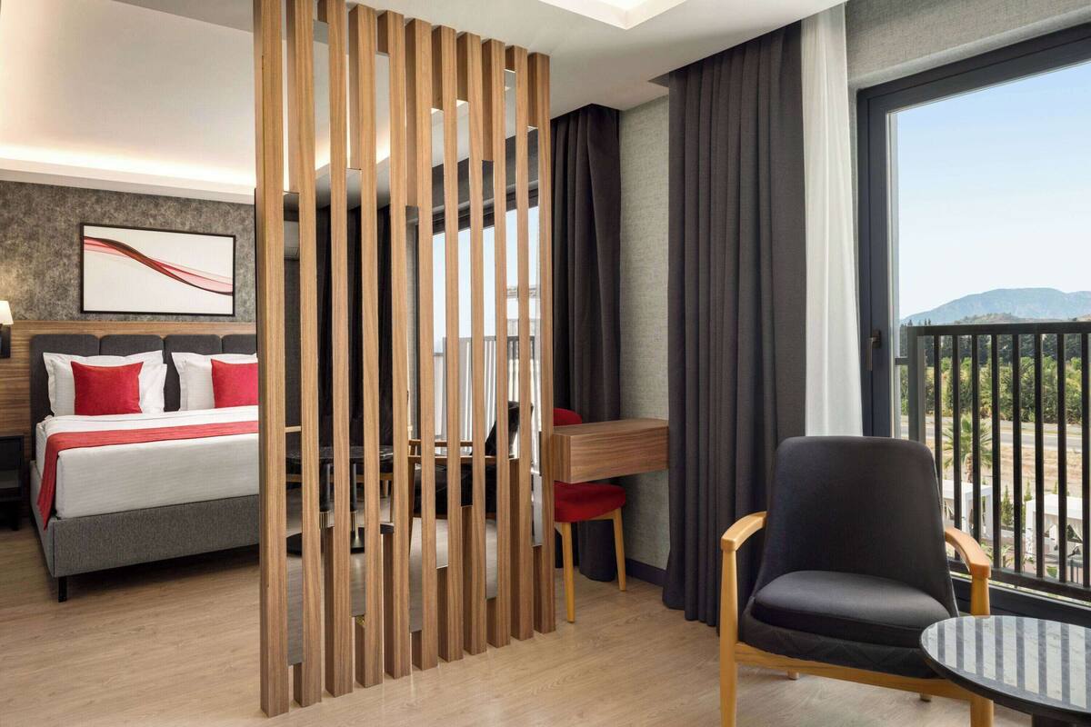 Een hotelkamer met een bed, een bureau, een stoel en een balkon met uitzicht.